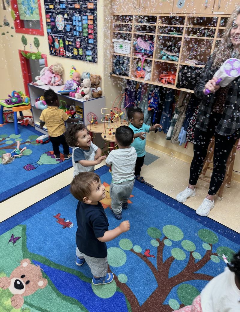 Toddlers playing together on the tree rug, with a teacher nearby.