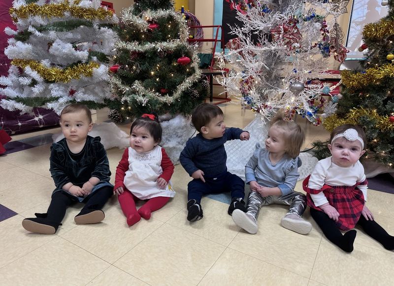 Our little ones sitting together in front of the holiday trees.