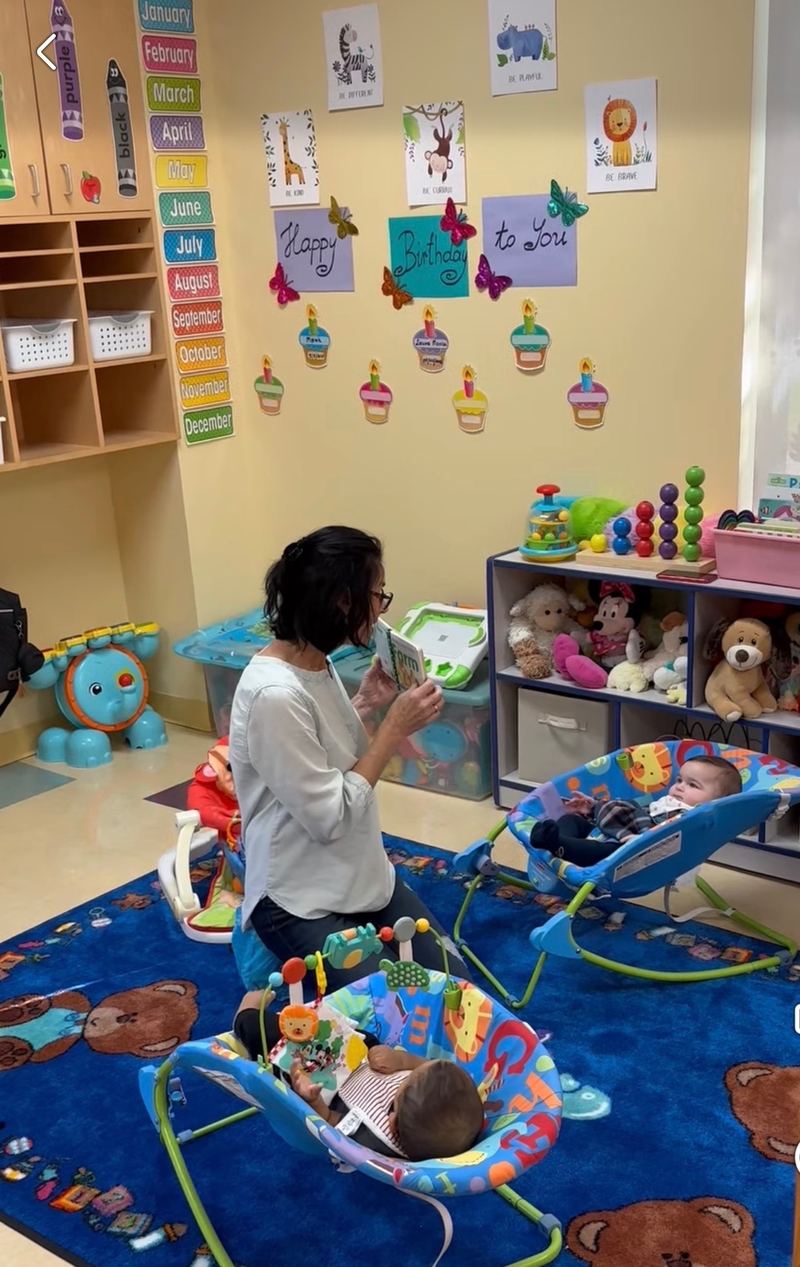A teacher with babies in bouncy seats on the teddy bear rug.