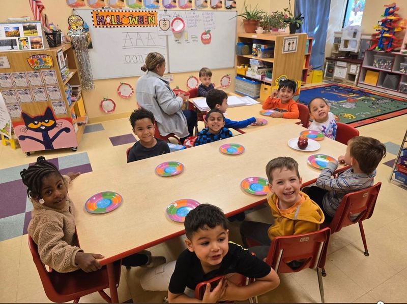 Children seated together at classroom tables for an activity with their teacher.