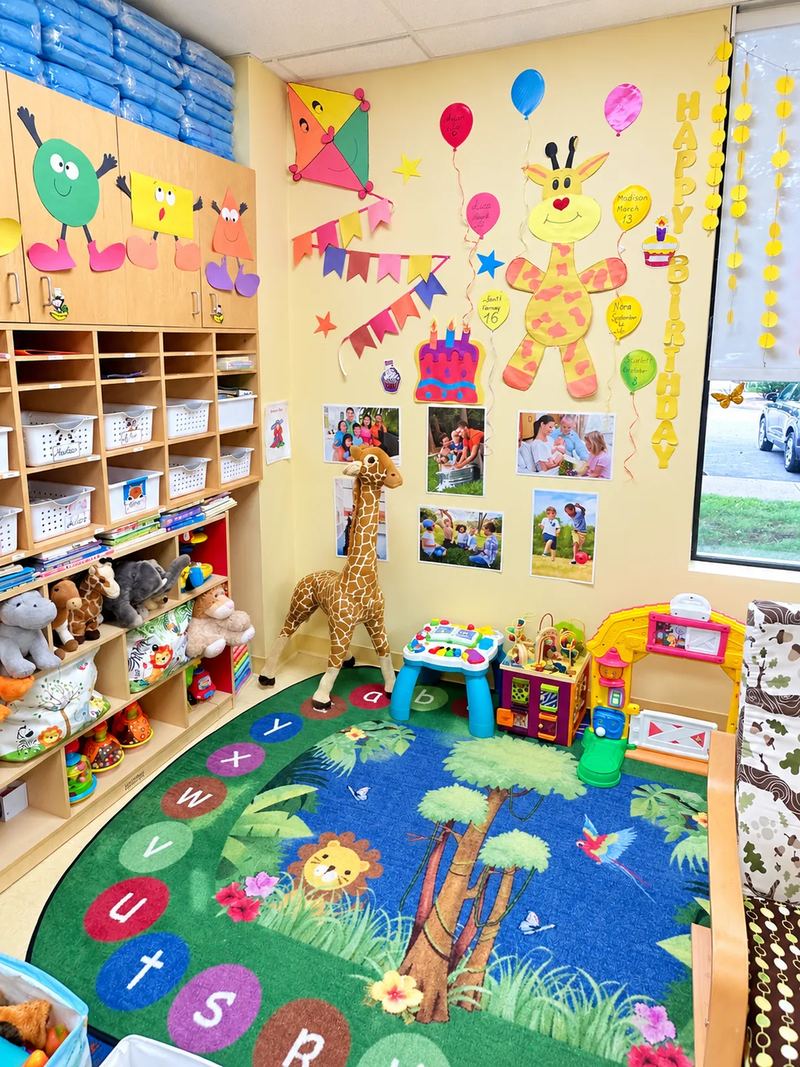 A birthday wall and family photo display above a jungle alphabet rug, with cubbies and stuffed animals along the wall.
